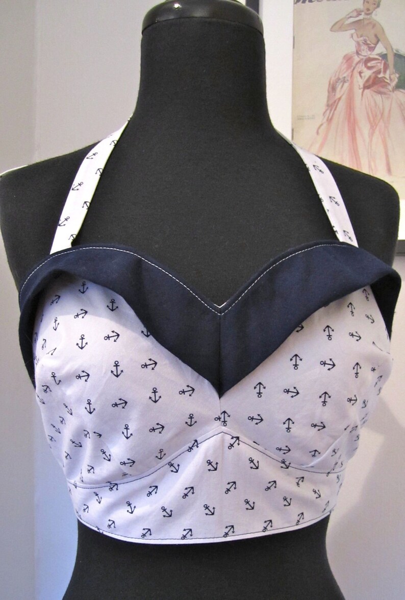 May include: A white halter top with a navy blue trim and a pattern of small anchors. The top is made of a soft, lightweight fabric and has a relaxed fit.