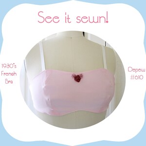 May include: A pink 1930's French bra with white straps and a floral embellishment in the center. The bra is displayed on a white dress form. See it sewn! Depew #610