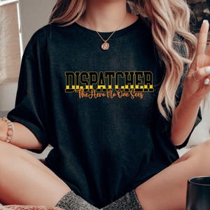 May include: A black t-shirt with the text "DISPATCHER The Hero No One Sees" in yellow and black lettering.