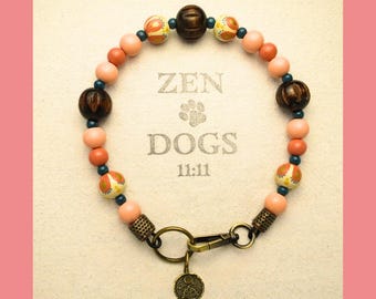 May include: A pink, brown, and blue beaded dog collar with a brass clasp and a charm. The collar has the words "ZEN DOGS 11:11" printed on it.