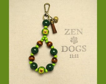 May include: A green and brown wooden bead keychain with a sunflower design. The keychain has a metal clasp and a small tassel. The keychain has the text "ZEN DOGS 11:11" on it.