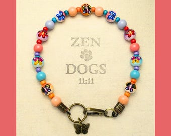 May include: A colorful dog collar with a butterfly charm. The collar features a variety of beads in shades of pink, orange, blue, and purple. The text "ZEN DOGS 11:11" is visible in the background.