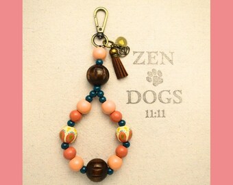May include: A beaded keychain with a gold clasp, featuring peach, dark brown, and teal beads. The keychain has a small brown tassel and a charm. The background has the text "ZEN DOGS 11:11".