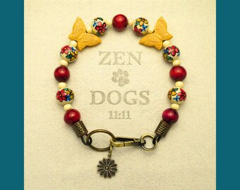May include: A dog collar with a mix of red, cream, and floral beads, along with two yellow butterfly accents. The collar has a metal clasp and a flower charm. The text "ZEN DOGS 11:11" is printed on the background.