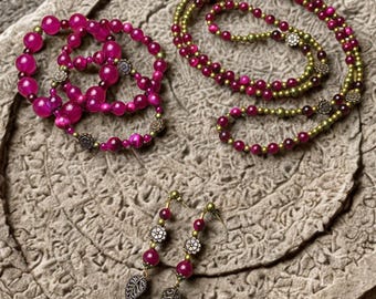 May include: A jewelry set consisting of a multi-strand bracelet, a long necklace, and a pair of drop earrings. The pieces feature vibrant magenta and olive green beads accented with small, round, metallic floral spacers and leaf-shaped charms.