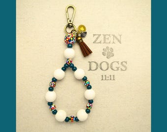 May include: A handmade keychain with a gold-tone clasp and a teardrop-shaped beaded design. The keychain features white and colorful beads, a brown tassel, and the text "ZEN DOGS 11:11" on the background.