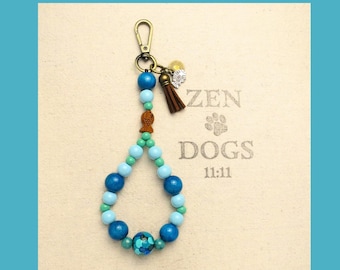 May include: A beaded keychain with blue, turquoise, and green beads, a brown tassel, and a gold-colored clasp. The keychain has a fish-shaped charm and the text "ZEN DOGS 11:11" on the background.