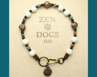 May include: White beaded dog collar with a colorful patterned bead, a gold clasp, and a gold charm with a symbol. The collar has the text "ZEN DOGS 11:11" printed on it.