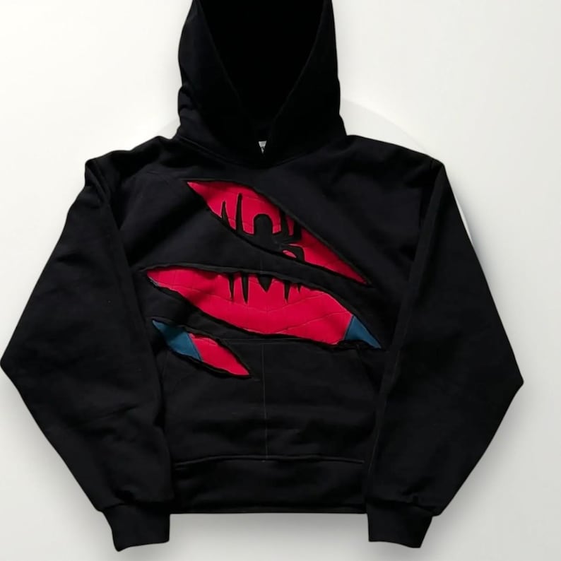 May include: Black hooded sweatshirt with a torn design revealing red and blue accents. The hoodie features a front pocket and a drawstring hood. The design gives the impression of a ripped or torn fabric, with a graphic element visible.