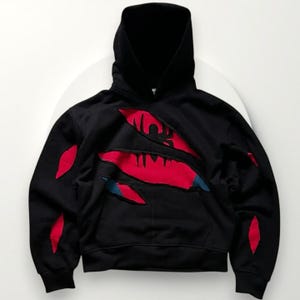 May include: Black hooded sweatshirt with a torn design revealing a red and blue graphic. The sweatshirt features a hood and a kangaroo pocket. Red accents are placed on the sleeves and chest, creating a unique visual effect.