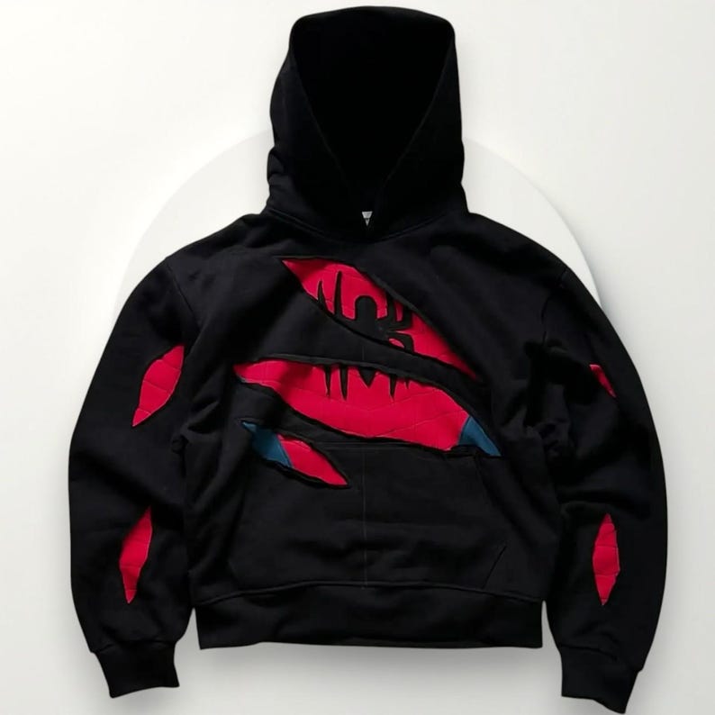 May include: Black hooded sweatshirt with a torn design revealing a red and blue graphic. The sweatshirt features a hood and a kangaroo pocket. Red accents are placed on the sleeves and chest, creating a unique visual effect.