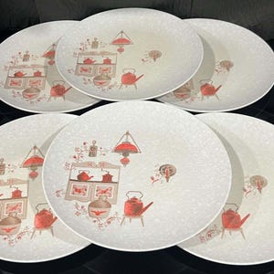May include: A set of five round dinner plates with a speckled off-white finish. Each plate features a printed graphic of a kitchen hutch, a hanging lamp, and a red tea kettle, accompanied by small floral accents and a ceramic jug.