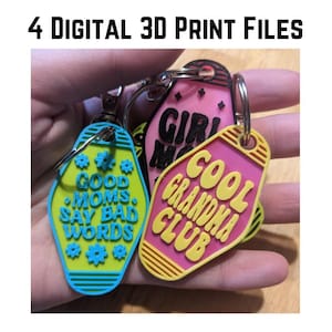 May include: Four colorful keychains with different phrases. The keychains are shaped like motel key tags. The phrases are "Good Moms Say Bad Words", "Cool Grandma Club", "Girl Mom", and "Cool Grandma Club".