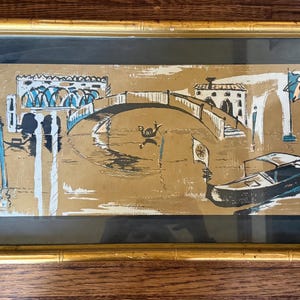 May include: An art print depicting a Venetian scene with a bridge, buildings, and a gondola. The artwork features gold, black, white, and teal colors. The print is framed in a gold bamboo-style frame with a black mat.