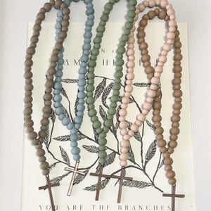 May include: Four wooden bead necklaces with a cross charm. The necklaces are in shades of brown, blue, green, and pink.