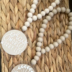 May include: Two decorative beaded garlands with round, light-colored beads. Each garland has a circular charm with white text. One charm reads "Pray More Worry Less," and the other says "Jesus Vibes."