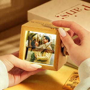 May include: A wooden photo cube with a rotating picture of a couple. The cube has the text "My heart is always te Amo!" and a small gold-colored button. The cube is held in a person's hands.
