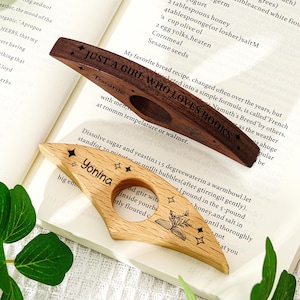 May include: Two wooden book page holders. One is dark brown with the text "JUST A GIRL WHO LOVES BOOKS" and stars. The other is light wood with the name "Yonina" and a book illustration.