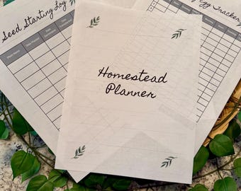 May include: Several printed planner pages with handwritten text. The pages are labelled "Seed Starting Log", "Observations", "Monthly Egg Tracker", and "Homestead Planner". Each page features a leaf design. The pages are arranged on a surface with green leaves.