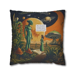 May include: A square cushion featuring a colourful illustration of a green alien and a woman standing in a field of plants. The background is a dark blue sky with stars and planets. The text "Ok, so your tinder pics are old huh?" is in a white speech bubble.