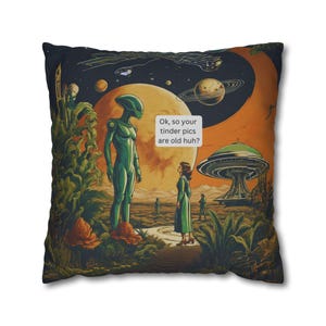 Peut inclure: Un coussin carré illustrant une scène spatiale colorée avec un extraterrestre vert et une personne debout sur une planète. Une bulle de dialogue contient le texte : Ok, so your tinder pics are old huh ? Le fond montre des planètes, une soucoupe volante et de la végétation.