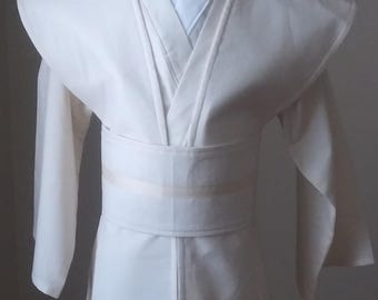 May include: A white robe with a long, flowing design. The robe has a wide collar and a belt that ties at the waist. The robe is made of a soft, lightweight fabric.