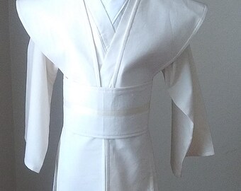 May include: A white, long-sleeved robe with a wide collar and a sash tied at the waist. The robe is made of a lightweight fabric and has a simple, elegant design.
