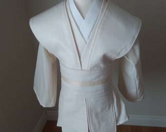 May include: A white, long-sleeved robe with a wide collar and a sash. The robe is on a mannequin.
