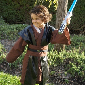 May include: A young child dressed as Darth Vader from Star Wars. They are wearing a brown and black robe with a black belt and holding a blue lightsaber.