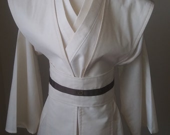 May include: White robe with a brown belt and a square buckle. The robe has a V-neck and long sleeves.