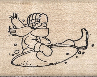 Puede incluir: Dibujo lineal en blanco y negro de una persona que se desliza en trineo. La persona lleva gorro, bufanda y guantes. La imagen está sobre un bloque de madera con una regla que muestra pulgadas, equivalentes a 2,54 cm.