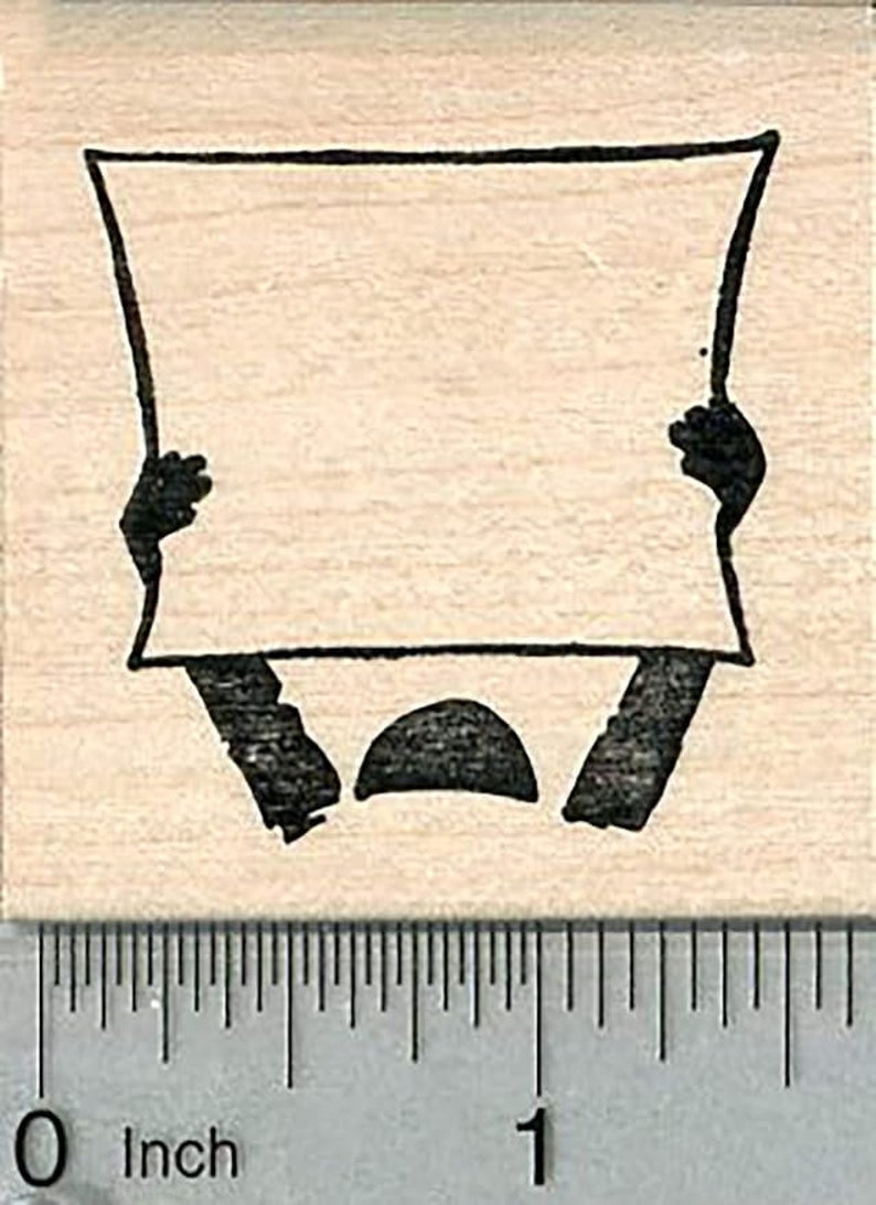 May include: A black and white rubber stamp featuring a simple line drawing of a person holding a blank sign. The sign is rectangular with rounded corners. The person is holding the sign with both hands, and the arms are bent at the elbows. The person's head is a simple circle.
