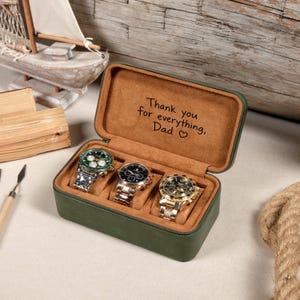 May include: A rectangular olive green watch storage case with a tan interior, holding three wristwatches on individual cushions. The inside lid features the engraved text: Thank you for everything, Dad with a small heart symbol included.