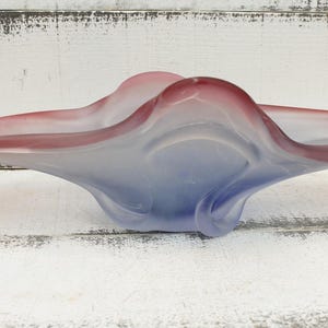 May include: A decorative glass bowl with a flowing, organic shape. The bowl transitions from a deep red at the edges to a soft blue in the center. The bowl is a unique piece of home decor.