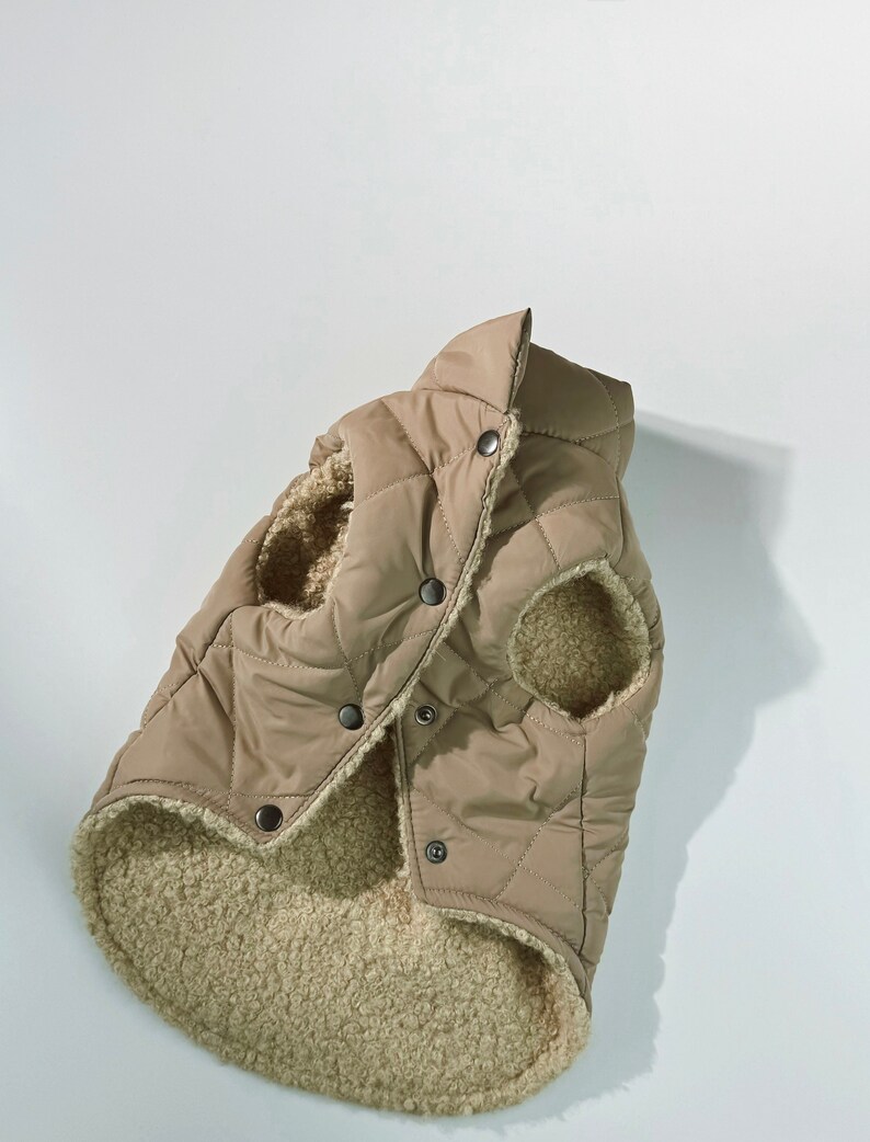 Puede incluir: Un chaleco acolchado beige para perros con un forro suave tipo sherpa. El chaleco tiene un patr&oacute;n de diamantes, cierre de botones y aberturas para las patas delanteras del perro. El cuello es alto.
