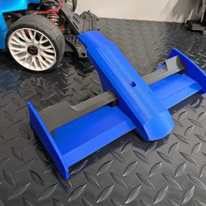 Pu&ograve; includere: Un'ala posteriore blu stampata in 3D per un'auto da corsa. L'ala ha due alette verticali e un'ala orizzontale con una barra di supporto nera.