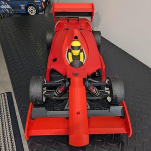 Pu&ograve; includere: Un'auto da corsa rossa con un sedile del conducente nero e un casco giallo. L'auto ha un grande alettone posteriore ed &egrave; seduta su una superficie nera.