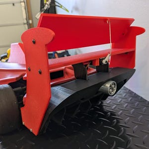 May include: A red and black toy race car with a large rear wing and a black exhaust pipe. The car has a detailed design and is made of plastic.
