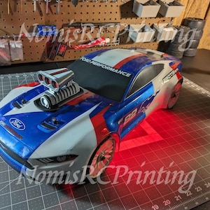 May include: A blue, white, and red Ford Performance race car with a custom supercharger and a red light reflecting off the body. The car has the text "PROTOform" and "B2" on the side.