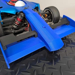 Pu&ograve; includere: Un'auto da corsa blu e nera con un grande alettone posteriore. L'auto ha un interno bianco e rosso ed &egrave; seduta su una superficie nera.