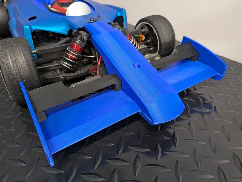 Pu&ograve; includere: Un'auto da corsa blu e nera con un grande alettone posteriore. L'auto ha un interno bianco e rosso ed &egrave; seduta su una superficie nera.
