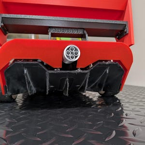 May include: A red and black model race car with a rear wing and exhaust pipes. The car has a black undercarriage and a red body. The exhaust pipes are silver.