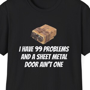 May include: Black t-shirt with the text "I HAVE 99 PROBLEMS AND A SHEET METAL DOOR AIN'T ONE." Above the text is a graphic of a brown object. The t-shirt has a crew neck and short sleeves.