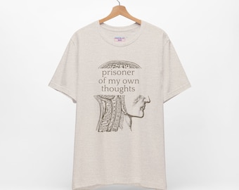 May include: A light beige t-shirt with a vintage anatomical illustration of a head and the text "prisoner of my own thoughts" printed on the front.