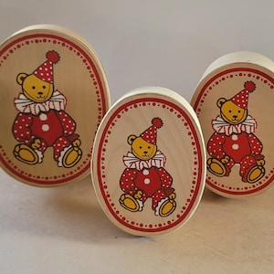 May include: Three wooden oval boxes with a light wood finish. Each box features a cartoon bear dressed as a clown in red and white polka dots, wearing a red party hat. The boxes are of varying sizes.