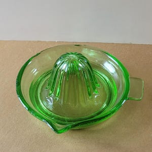 May include: Green glass citrus juicer with a ribbed center and a handle. The juicer is designed to squeeze lemons, limes, and oranges.