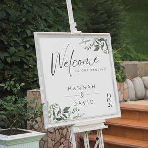 May include: White wedding welcome sign with green foliage and the text "Welcome to our wedding", "Hannah & David", and "14 09 24".
