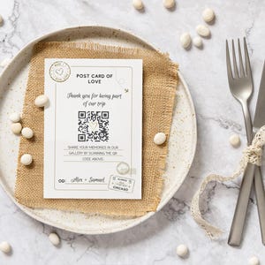 Może przedstawiać: Pocztówka z napisem "POST CARD OF LOVE" i kodem QR, umieszczona na talerzu z lnianą podkładką. Widelec i nóż są związane wstążką z koronki. Białe kamyki są rozrzucone.