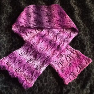 May include: A purple and white knitted scarf with a lacy pattern.
