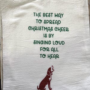 May include: White Christmas-themed kitchen towel with green text that reads "The best way to spread Christmas cheer is by singing loud for all to hear." A red glitter dog graphic is at the bottom.